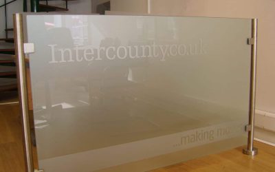 A glass barrier with metal poles featuring company logo and tagline