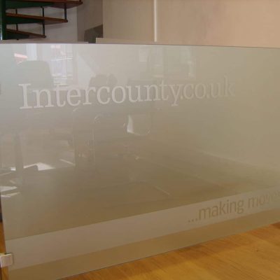 A glass barrier with metal poles featuring company logo and tagline